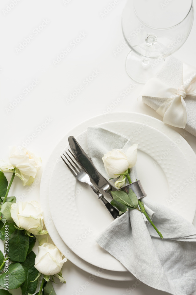 Romantic and wedding table setting with white rose, gift, dishware, silverware on white table. Top view. Romantic and wedding table setting with white rose, gift, dishware, silverware on white table. Top view.