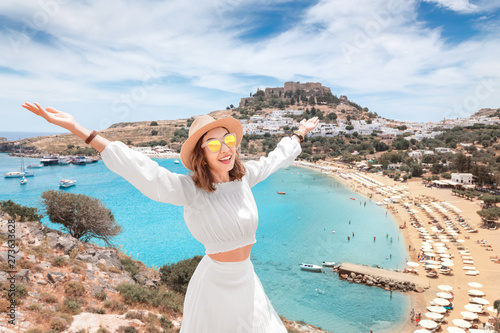 Happy asian woman raised hands travels in Greece. Having fun at the stunning view on sea resort and old town of Lindos on the mountain