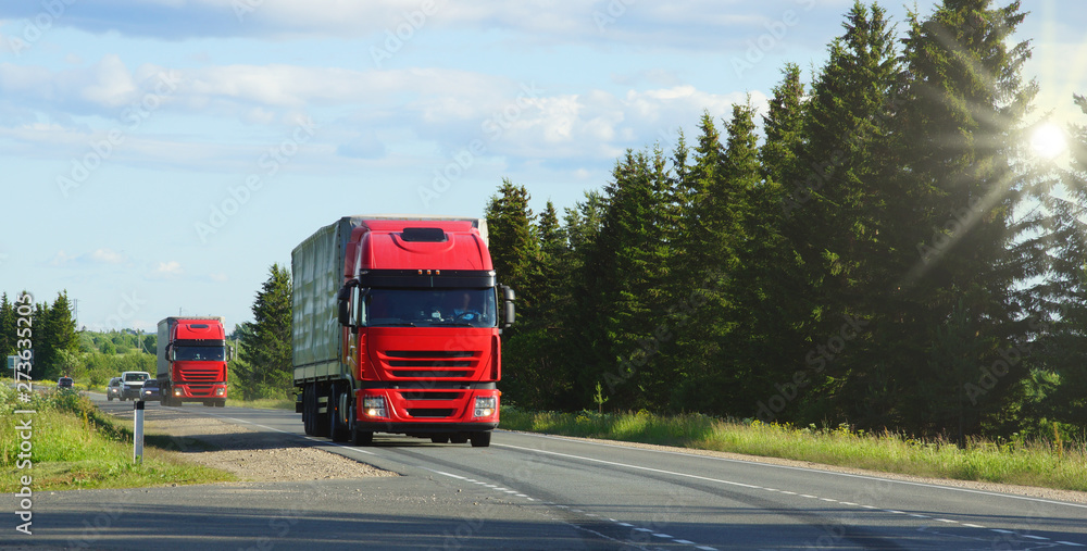 shipping two red cargo trucks on the road being driven sun rays