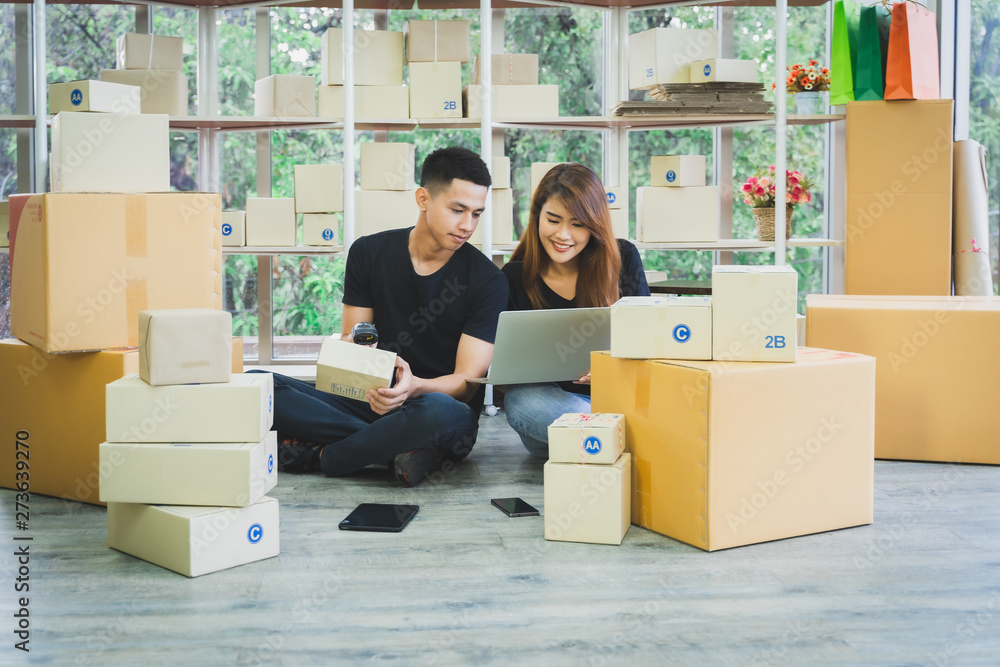 Young happy asian business couple is work together by using laptop, smartphone or tablet with a parcel box packaging at their startup home office, SME online business seller and delivery concept Young happy asian business couple is work together by using laptop, smartphone or tablet with a parcel box packaging at their startup home office, SME online business seller and delivery concept