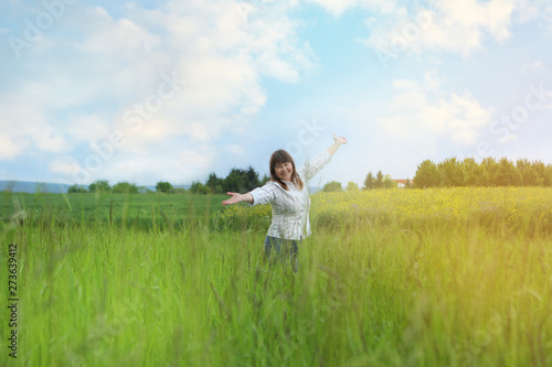 a woman in the field is standing enjoying nature, spreading her arms apart, uniting with nature