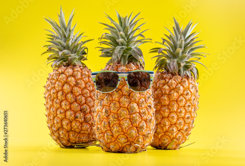 Creative pineapple looking up with sunglasses and shell isolated on yellow background, summer vacation beach idea design pattern, copy space close up