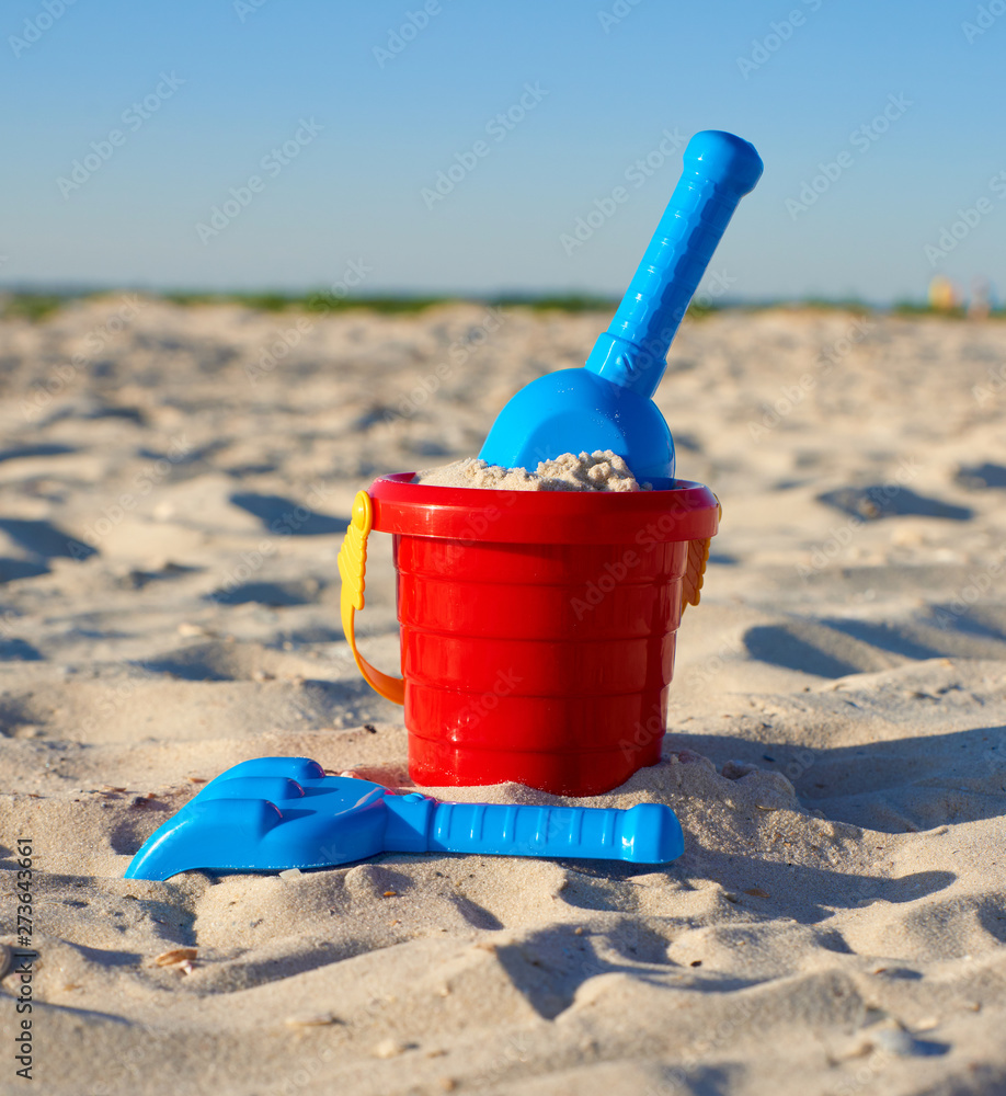 red plastic bucket and blue rake, shovel on the sand