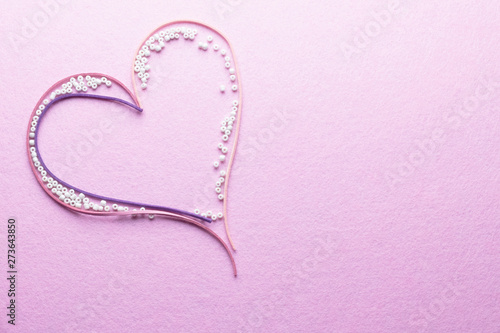 A heart as a love symbol made of pink and purple laces and white tiny beads on a pink background.