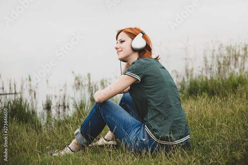 Young fashion girl with headphones sitting at lake coast. photo
