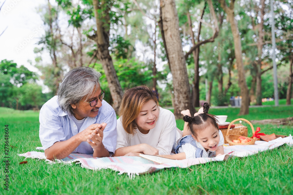 Fototapeta premium Asian grandparents and granddaughter are lying on the grass field outdoor, asian family concept