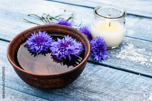 blue cornflowers lie in the water in a bowl near a burning candle on the background of the old blue boards.