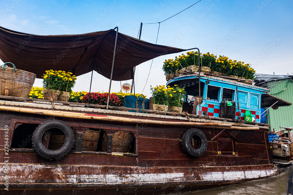 Brown and blue boat or sampan carrying yellow and red flowers for Tet New Year Celebration, Mekong Delta, Vietnam.