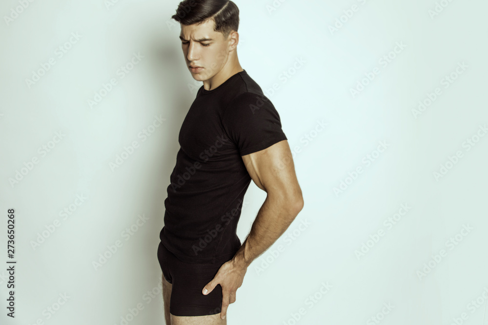 Strong stripped muscle male model in black underwear and black t-shirt on grey isolated font background Strong stripped muscle male model in black underwear and black t-shirt on grey isolated font background