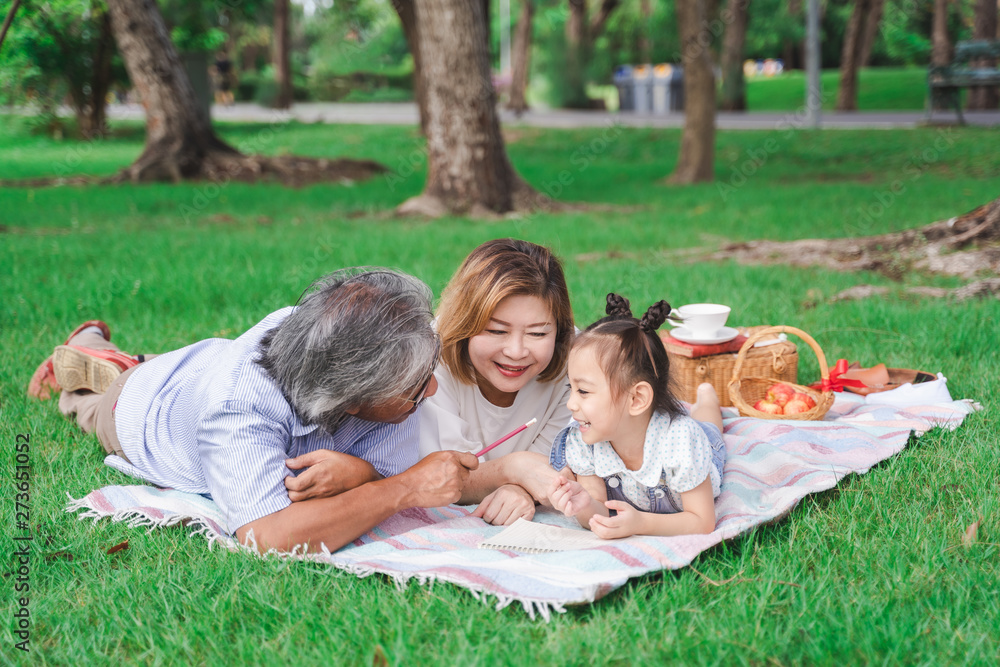 Asian grandparents and granddaughter are lying on the grass field outdoor, asian family concept