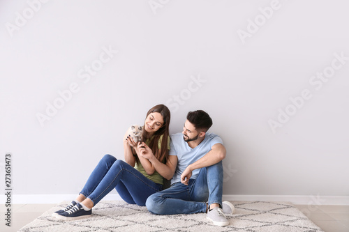 Young couple with cute kitten sitting near light wall