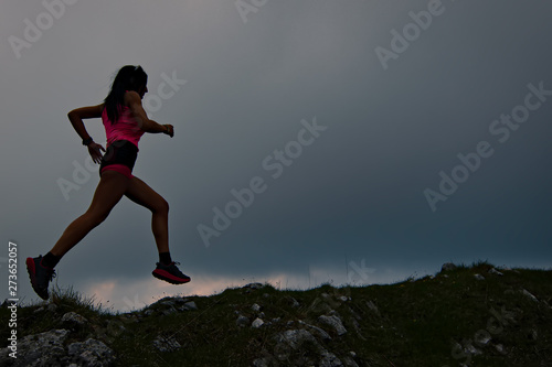 Sporty girl with beautiful athletic body runs in the alpine ridge at dusk