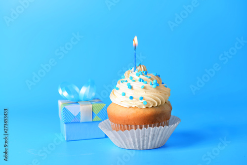 Tasty Birthday cupcake with gift box on color background