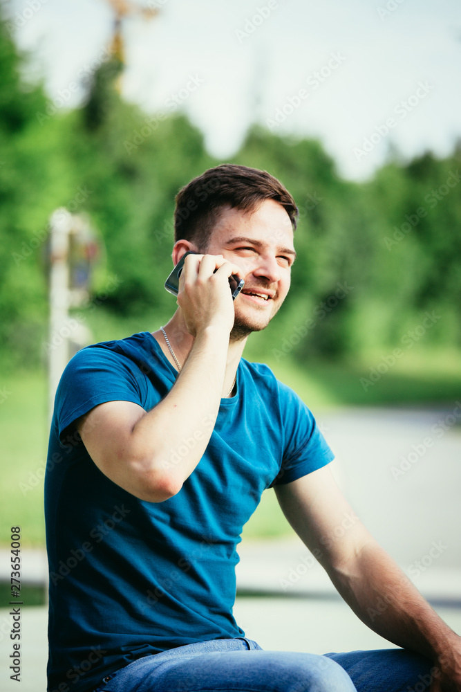 Young man calling outdoors: Handsome young man is sitting and calling, summertime Young man calling outdoors: Handsome young man is sitting and calling, summertime