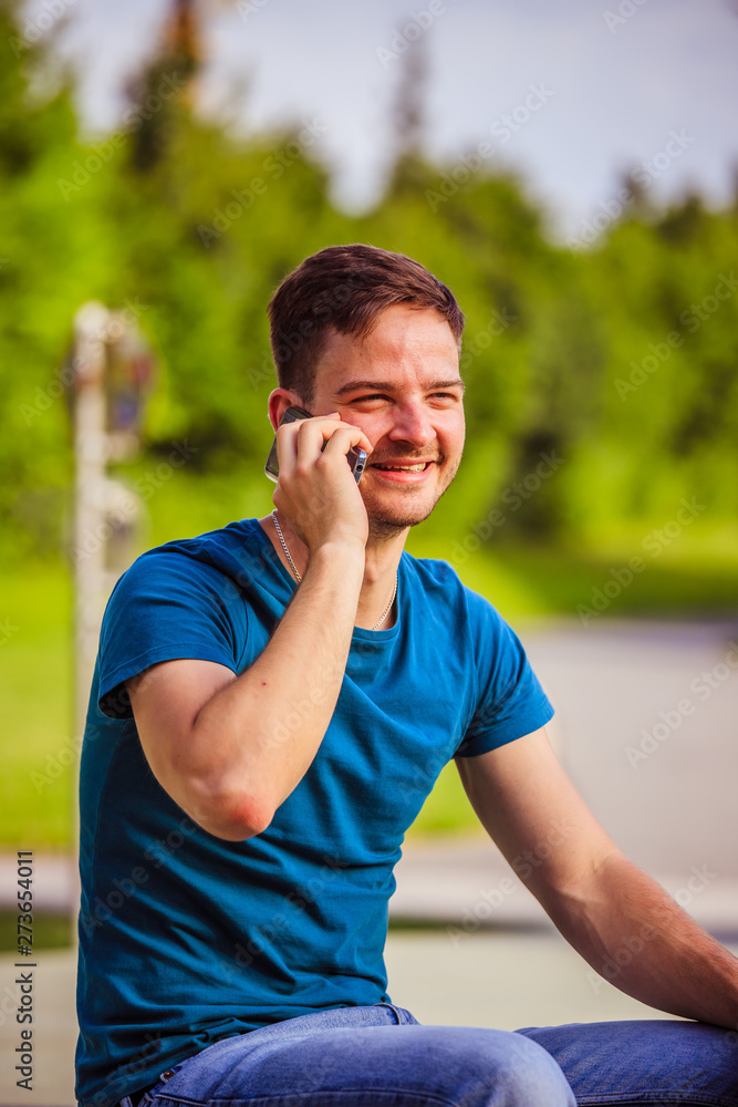 Young man calling outdoors: Handsome young man is sitting and calling, summertime Young man calling outdoors: Handsome young man is sitting and calling, summertime