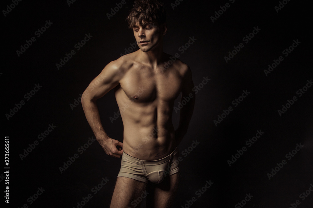 Strong stripped muscle male model in beige underwear on black isolated font background Strong stripped muscle male model in beige underwear on black isolated font background