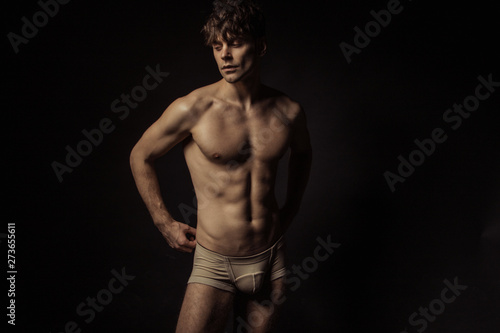 Strong stripped muscle male model in beige underwear on black isolated font background