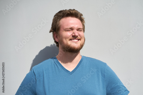 Caucasian bearded young man in blue t-shirt laughing in sunlight with closed eyes