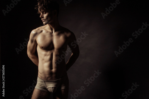 Strong stripped muscle male model in beige underwear on black isolated font background