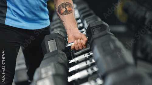 Muscular male arm picking up heavy dumbbell from equipment rack