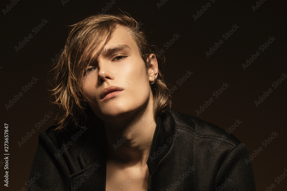 Muscle blonde beautiful stripped male model with long hair in black suit on beige brown isolated font background Muscle blonde beautiful stripped male model with long hair in black suit on beige brown isolated font background