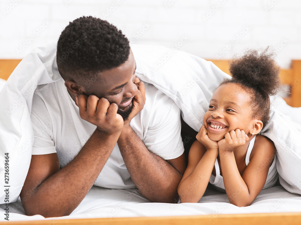 Cute african dad and daughter lying on bed and smiling to each other Cute african dad and daughter lying on bed and smiling to each other