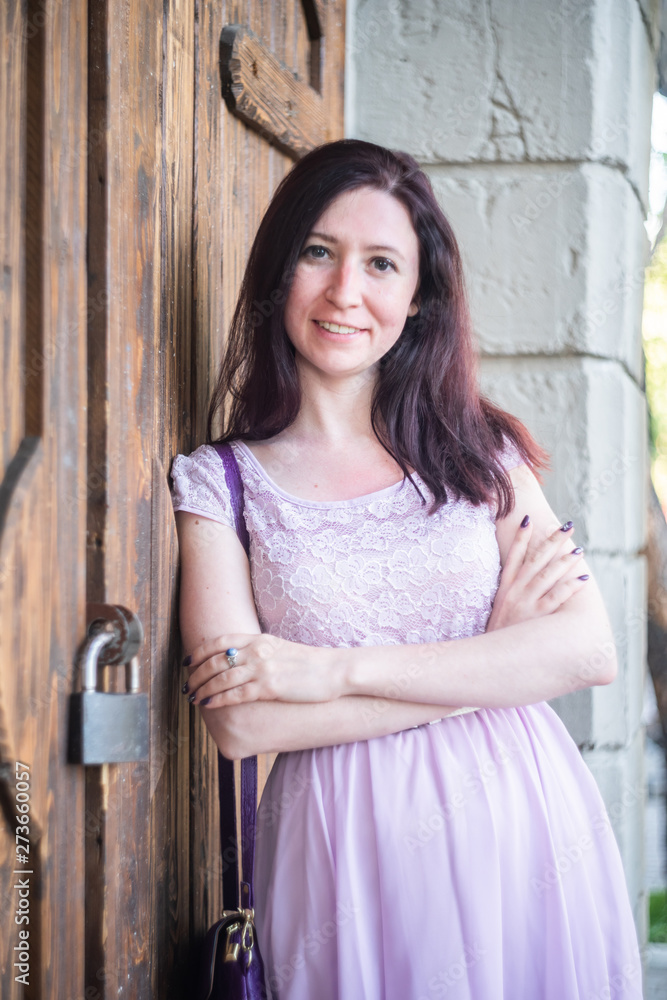 Young happy smiling caucasian woman in a summer dress leaning against the door outdoors Young happy smiling caucasian woman in a summer dress leaning against the door outdoors