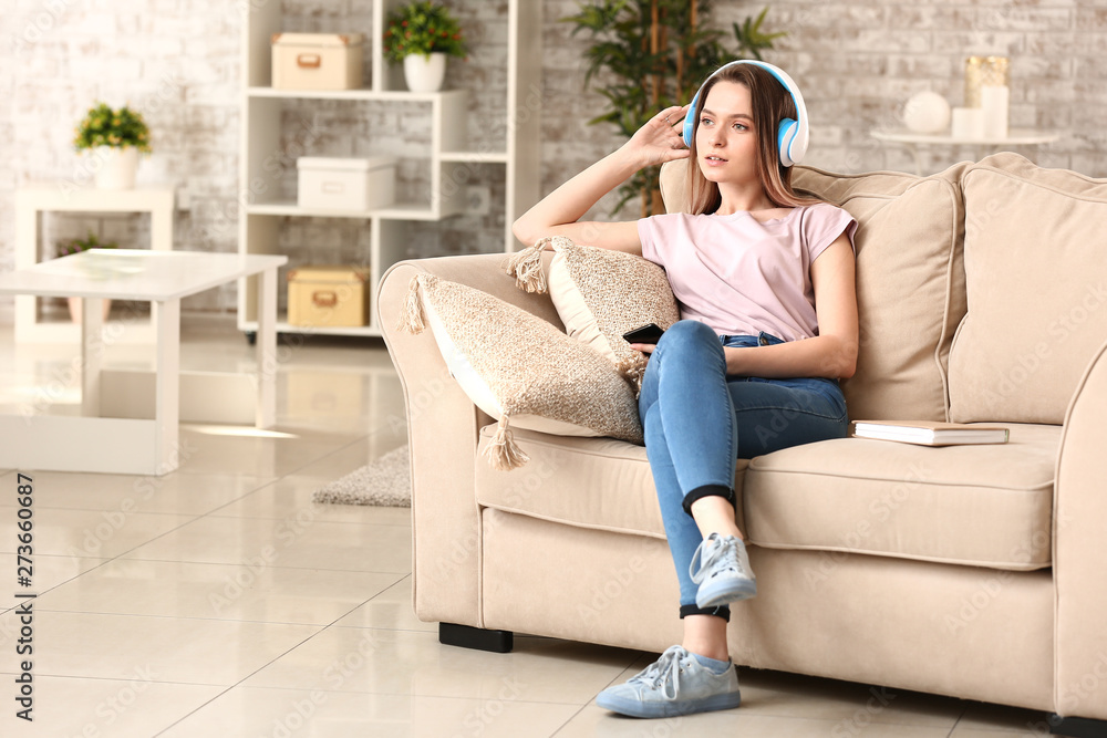 Obraz premium Beautiful young woman listening to audiobook while sitting on sofa at home
