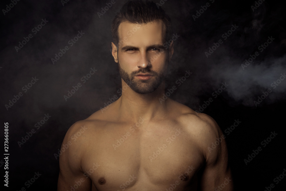 Handsome sport sexy stripped guy portrait in a water draps and fog smoke mist on isolated black background