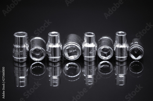 A set of steel tools with reflection in glass on a contrasting black background.