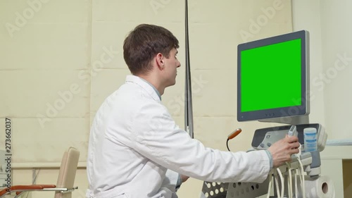 Male doctor using ultrasound scanner with chroma key screen. Happy friendly male physician smiling to the camera, operating ultrasound scanner with green screen. Medicine concept photo