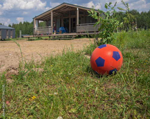 Red soccer ball for children on the green grass in front of a country house. Space for text