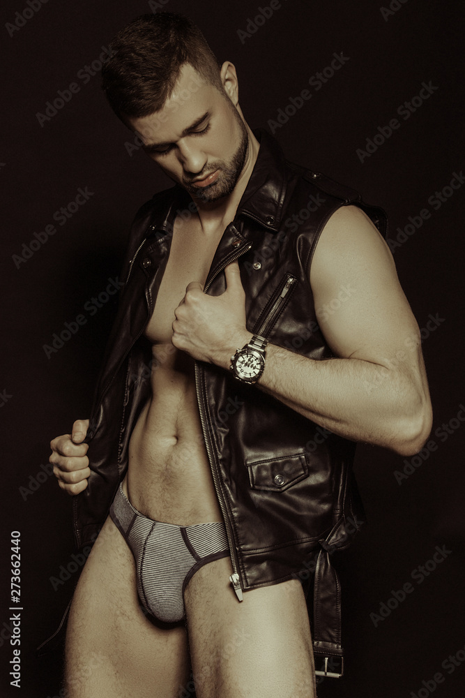 Muscle strong beautiful stripped male model in black leather jacket and underwear on black isolated font background