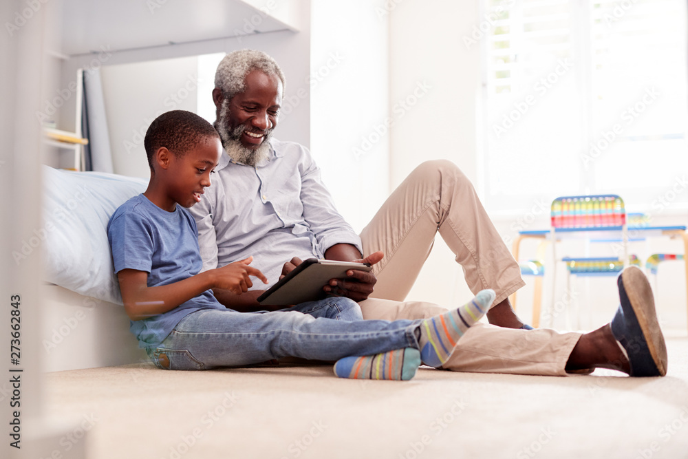 Grandfather Sitting With Grandson In Childs Bedroom Using Digital Tablet Together