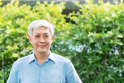 Headshot of happy old mature asian with white grey hair man wearing blue shirt smiling positive and looking at camera in garden outside the house. Senior asian male portrait with retirement concept.