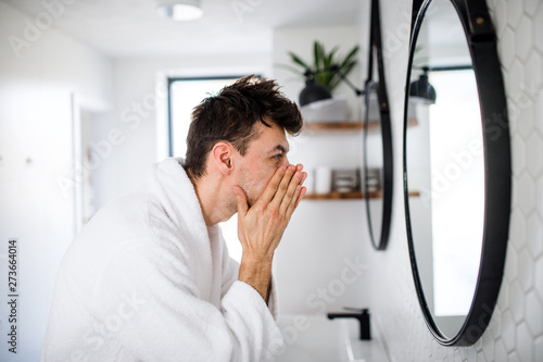Young man washing face in the bathroom in the morning, daily routine.