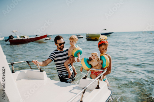 Parents with two small toddler children standing by boat on summer holiday.