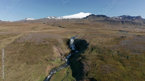 Eye level shot of snowy mountain with waterfall and canyon in the foreground, forward drone camera movement photo