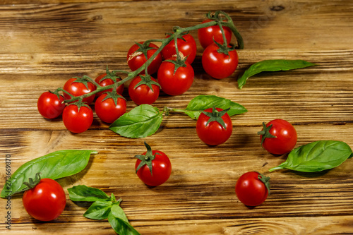 Fresh cherry tomatoes with green basil leaves on a wooden table