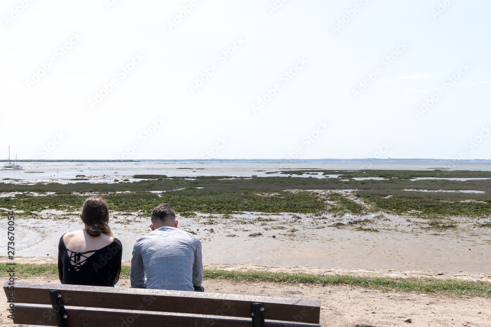 Man and woman couple sitting on beach and watching calm low tide sea