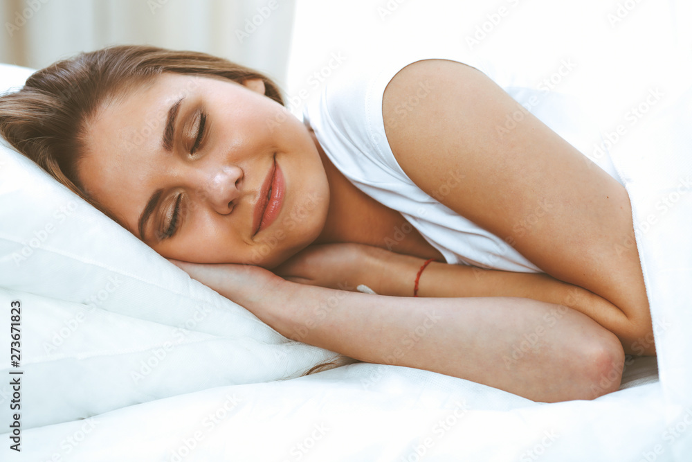 Beautiful young and happy woman sleeping while lying in bed comfortably and blissfully smiling Beautiful young and happy woman sleeping while lying in bed comfortably and blissfully smiling