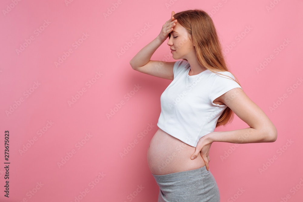 Young pregnant woman with a headache, on a pink background Young pregnant woman with a headache, on a pink background