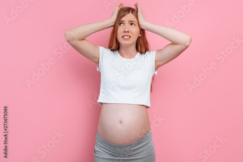 Young pregnant woman with a headache, on a pink background