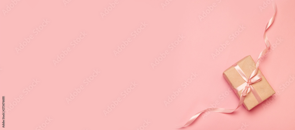 Top view of a gift wrapped as a gift kraft paper decorated with a ribbon on a pink background - obrazy, fototapety, plakaty 