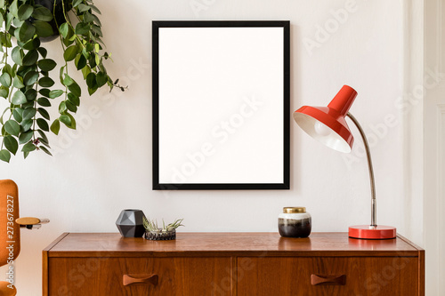 Stylish room of home interior with brown mock up frame with vintage accessories, plant, orange chair and red retro table lamp. Cozy home decor. Minimalistic concept. Modern composition of cupboard. © FollowTheFlow