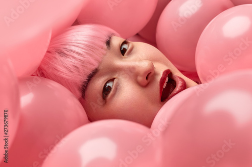 Amazed Asian woman under pink balloons