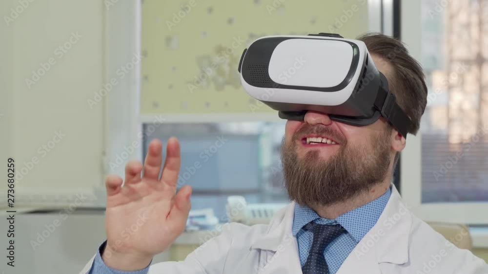 Male doctor using 3d virtual reality glasses at the hospital. Cropped shot of a bearded practitioner enjoying using vr headset at work. Medical technology, modern science concept Male doctor using 3d virtual reality glasses at the hospital. Cropped shot of a bearded practitioner enjoying using vr headset at work. Medical technology, modern science concept