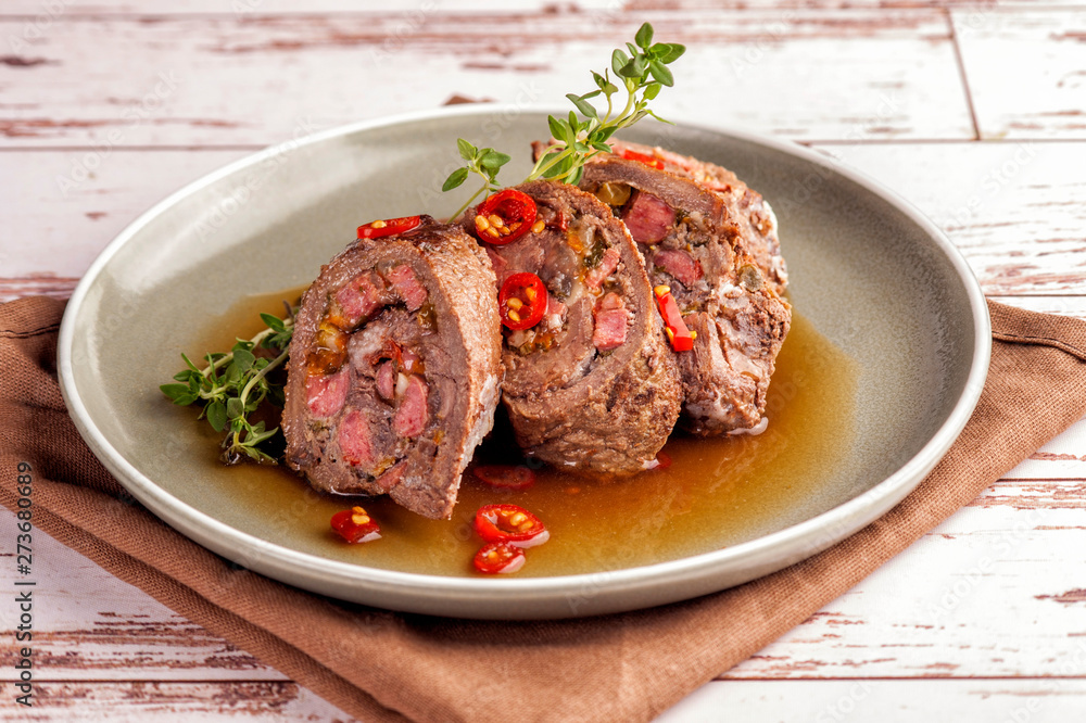 Beef tenderloin rolls stuffed. Slices of meat served on a plate in a sauce and with fresh vegetables and herbs. Close up and horizontal orientation. Beef tenderloin rolls stuffed. Slices of meat served on a plate in a sauce and with fresh vegetables and herbs. Close up and horizontal orientation.