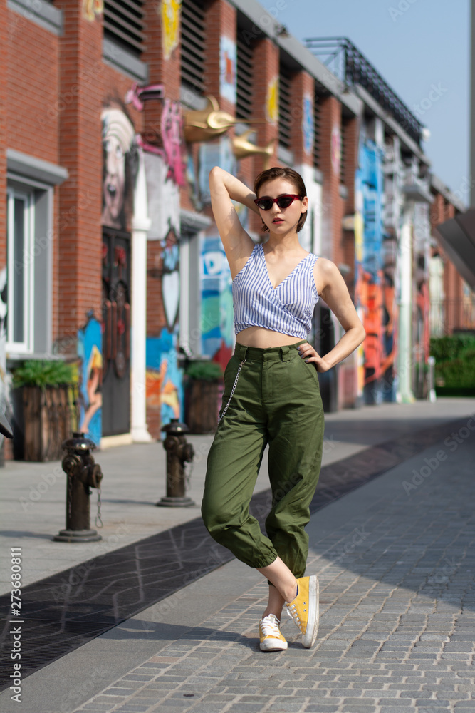 Asian Chinese model girl influencer street shot. Wearing Blue top and army green pants. Street Graffiti background.