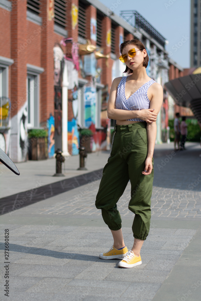 Asian Chinese model girl influencer street shot. Wearing Blue top and army green pants. Street Graffiti background.